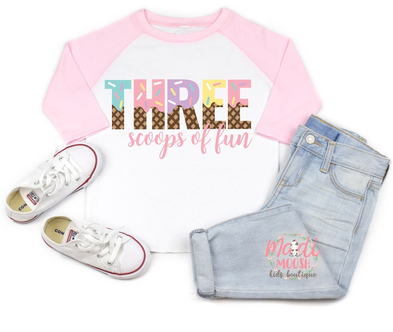 May include: A white and pink baseball tee shirt with the text "THREE scoops of fun" in colorful ice cream cone letters. The shirt has a pink and white color block design.