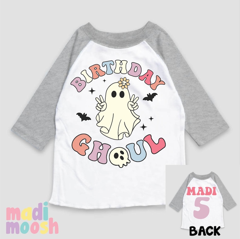 May include: A white and grey raglan t-shirt with a colourful "Birthday Ghoul" graphic featuring a ghost with a flower on its head. The back of the shirt has a pink number "5" and the word "Madi" in pink.