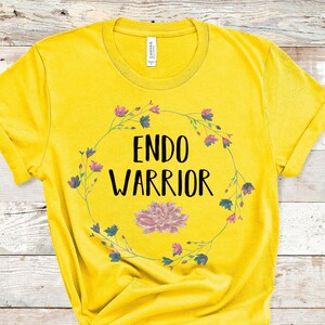 May include: Yellow t-shirt with a floral wreath design and the text "ENDO WARRIOR" in black.