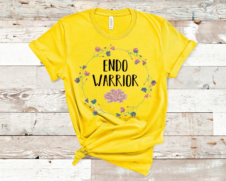 May include: Yellow t-shirt with a floral wreath design and the text "ENDO WARRIOR" in black.