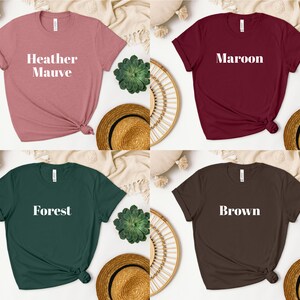 May include: Four t-shirts in different colors with the color name printed in white on the front. The colors are Heather Mauve, Maroon, Forest, and Brown.