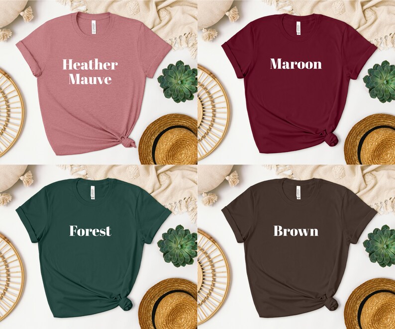 May include: Four t-shirts in different colors with the color name printed in white on the front. The colors are Heather Mauve, Maroon, Forest, and Brown.