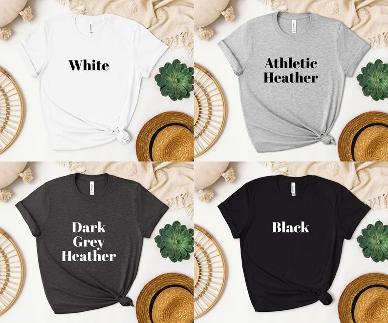 May include: Four t-shirts in different colors: white, athletic heather, dark grey heather, and black. Each shirt has a different text printed on the front: "White", "Athletic Heather", "Dark Grey Heather", and "Black".