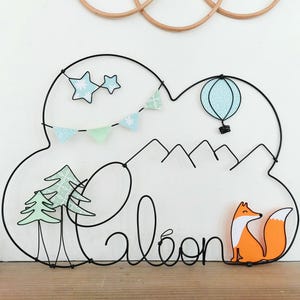 May include: Black wire art sculpture of a cloud with a hot air balloon, stars, and a string of flags. The cloud also has the name "Leon" written in wire and a small orange fox figurine.