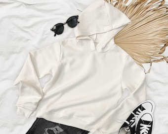 May include: A white hooded sweatshirt with long sleeves, black jeans with distressed details, black sunglasses, and black trainers with white soles.