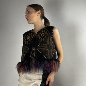 May include: A black vest with geometric patterns in brown and gold, embellished with small beads and a tassel. The vest features colorful faux fur trim in shades of purple, blue, and orange. The vest is sleeveless.