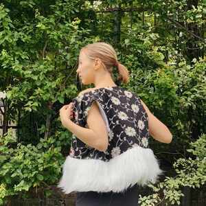 Pu&ograve; includere: Un gilet nero e bianco a fiori con un bordo in pelliccia sintetica bianca. Il gilet &egrave; senza maniche e ha una scollatura rotonda.