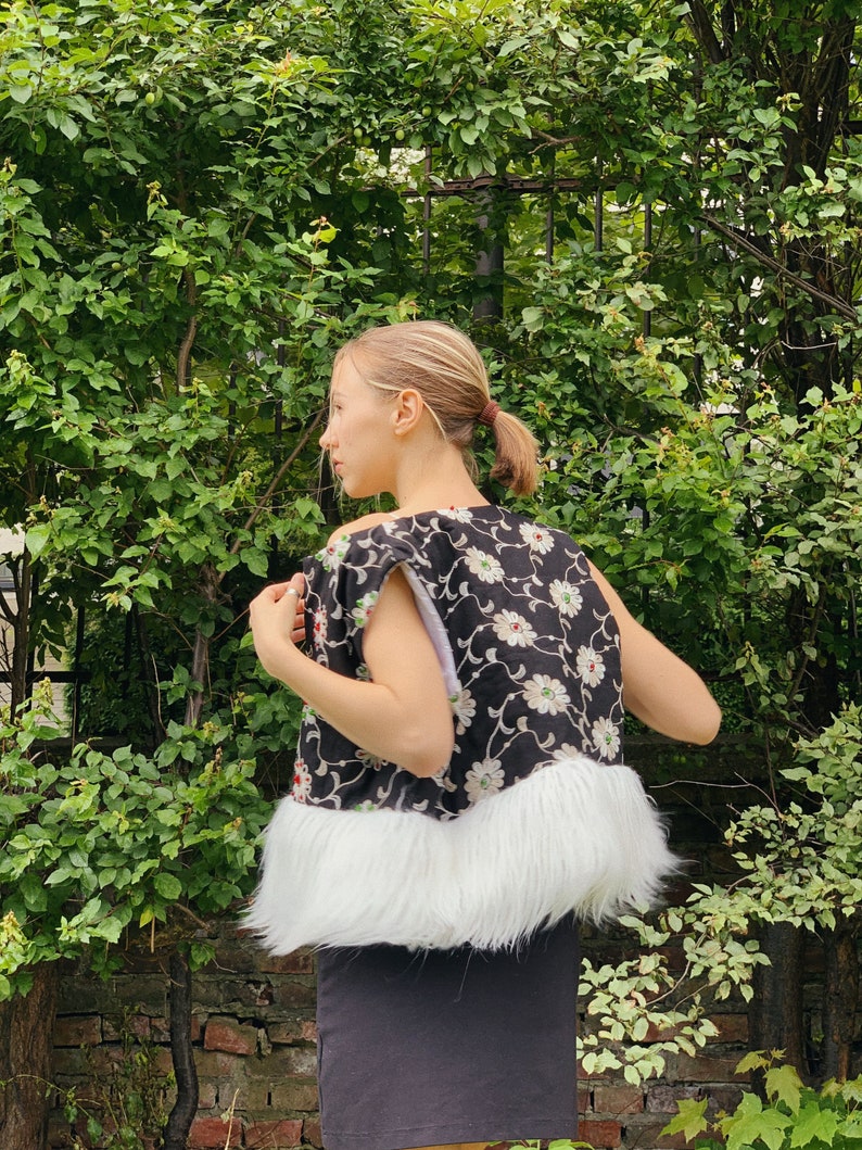 Pu&ograve; includere: Un gilet nero e bianco a fiori con un bordo in pelliccia sintetica bianca. Il gilet &egrave; senza maniche e ha una scollatura rotonda.