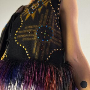 May include: A black vest with a geometric design in gold and embellished with colorful beads. The vest has a faux fur trim in shades of purple, blue, and orange. The vest is sleeveless.