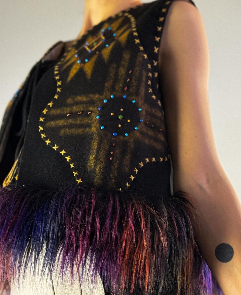 May include: A black vest with a geometric design in gold and embellished with colorful beads. The vest has a faux fur trim in shades of purple, blue, and orange. The vest is sleeveless.