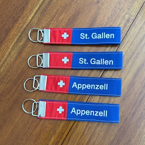 May include: Four keychains with a red and white Swiss flag design and the text "St. Gallen" and "Appenzell" in white lettering on a blue background. Each keychain has a silver metal ring.