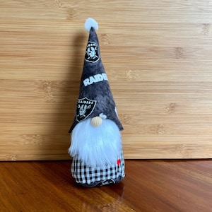 May include: A black and white gnome with a white beard and a black and white checkered skirt. The gnome is wearing a black and white hat with the word "RAIDERS" on it.