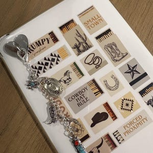 May include: A silver charm bracelet with cowboy-themed charms, including a cowboy hat, boot, and turquoise and red accents. The bracelet is attached to a white phone case decorated with Western-style illustrations and the text "COWBOY HAT RULE".