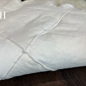 May include: White faux fur rug with a diamond-shaped stitching pattern. The rug is folded in half and the stitching is visible on the fold.