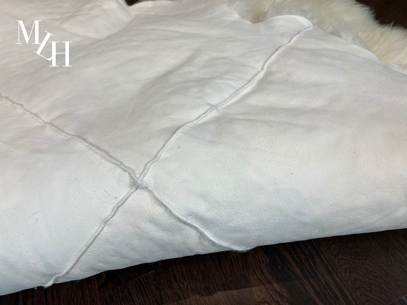 May include: White faux fur rug with a diamond-shaped stitching pattern. The rug is folded in half and the stitching is visible on the fold.