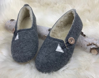 May include: A pair of grey wool slippers with a white triangle and a wooden button on each. The slippers have a white fleece lining.