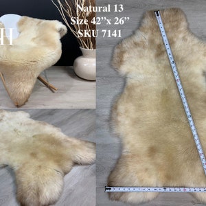 May include: Natural sheepskin rug in a light beige color. The rug is 42 inches by 26 inches and has a soft, fluffy texture. The rug is shown in three different positions, including on a wooden chair, on a wooden floor, and laid flat with a measuring tape.