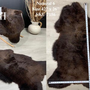 May include: A brown sheepskin rug with a natural color. The rug is 42 inches by 26 inches and has the SKU 7156. The rug is laid out flat on a light brown surface with a measuring tape next to it.