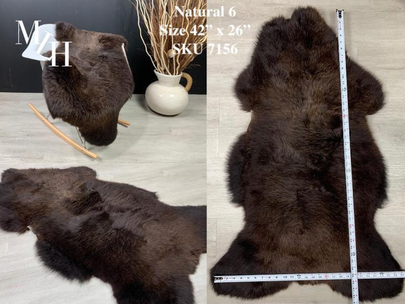May include: A brown sheepskin rug with a natural color. The rug is 42 inches by 26 inches and has the SKU 7156. The rug is laid out flat on a light brown surface with a measuring tape next to it.