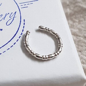 May include: A silver ear cuff with a beaded design. The cuff is on a white box with the text "Bit Gallery" in blue.