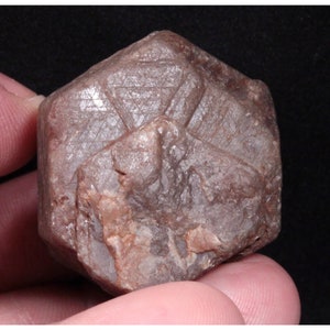 May include: A large, dark red, rough, natural ruby crystal with a hexagonal shape. The crystal has a striated surface and is a beautiful example of a natural gemstone.
