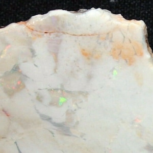 May include: A rough, white opal with a light orange hue and iridescent flashes of green and red.