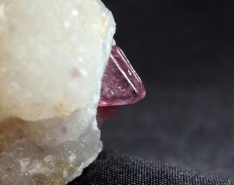 May include: A pink, triangular shaped crystal embedded in a white, rocky matrix.