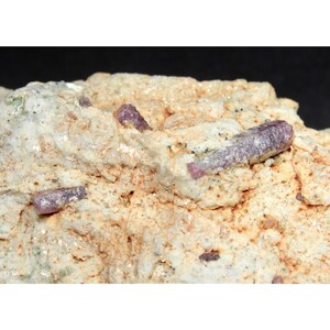 May include: A close-up of a rock with several small, pink ruby crystals embedded in it.