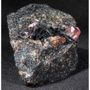 Puede incluir: Una roca gris oscura con dos cristales rosados incrustados. Los cristales son afilados y tienen un aspecto vítreo.