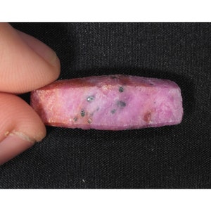以下が含まれることがあります： 黒いインクルージョンが入ったピンクのルビーの宝石。ルビーはファセットカットされており、長方形の形をしています。