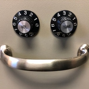 May include: A silver metal handle with two black knobs. The knobs have numbers 1-10 and the words "VOL." and "TONE" written on them.