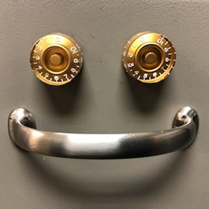 May include: A gray metal safe with two gold combination locks and a silver handle. The handle is shaped like a smile.