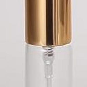 May include: A clear glass bottle with a gold-colored cap and a clear plastic pump. The bottle is cylindrical and appears to be empty. The cap is a shiny, metallic gold color. The pump extends into the bottle.