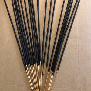 May include: A bundle of black incense sticks with wooden tips. The sticks are arranged in a fan shape on a brown surface.