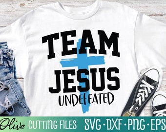 Puede incluir: Camiseta blanca con una cruz azul y el texto "Team Jesus Undefeated" en negro.