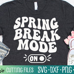 May include: A dark gray t-shirt with white text that reads "Spring Break Mode On". The text is in a retro font style with a toggle switch graphic.