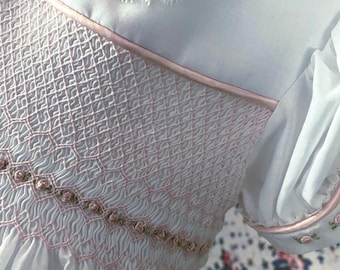 Romantische, ouderwetse gesmokte babyjurk in vintage stijl van witte Zwitserse voile. Roze rozen tussen roze smokwerk. Grootte: 6 tot 12 m.