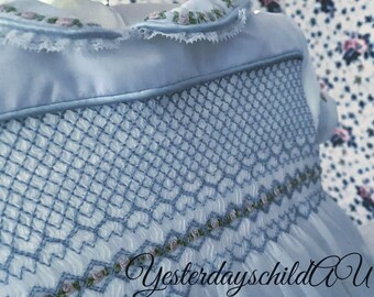 Romantische, ouderwetse gesmokte babyjurk in vintage stijl van witte Zwitserse voile.  Roze rozen tussen blauwe smokwerk. Grootte: 6 tot 12 m.