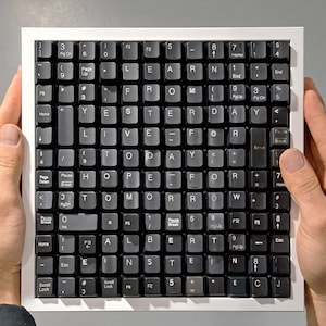 May include: A framed artwork composed of black computer keys spelling out "LEARN FROM YESTERDAY LIVE FOR TODAY HOPE FOR TOMORROW ALBERT EINSTEIN". The keys are set against a gray background within a white frame.