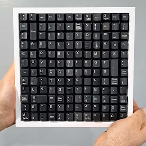 May include: A framed artwork made from black keyboard keys spelling out "IF YOU REALLY LOOK CLOSELY YOU SEE SUCCESS LONG TIME STEVE JOBS". The keys are set against a white frame.