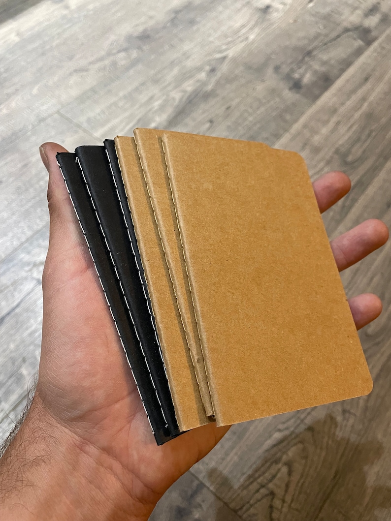May include: A stack of four notebooks, two with black covers and two with brown covers. The notebooks are bound with stitching along the spine.