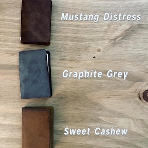 May include: Three leather notebooks in different colours: brown, grey, and brown. The notebooks are labelled "Mustang Distress", "Graphite Grey", and "Sweet Cashew".