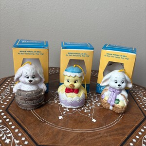 May include: Three bisque porcelain Easter bells with a bunny, chick, and lamb design. Each bell is in its original box with the text "Bisque Porcelain Bell As their feet swing, they ring!" on the front.