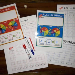 May include: Two colorful game boards for learning addition and subtraction. The boards feature spinners with numbers and instructions for rolling dice and finding the sum or difference. The boards are accompanied by a grid sheet and dry-erase markers.
