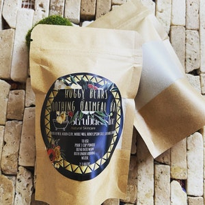 May include: A brown paper pouch with a label that reads "Huggy Bears Soothing Oatmeal Bath Scrubbie Sinc Natural Skincare". The label has a black and gold design with a small illustration of a bathtub. The text "To Use: Pour 1 cup powder blend into warm bath under running water 2-3 baths" is also on the label.