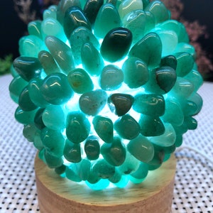 May include: A green gemstone lamp with a wooden base. The lamp is made of many small, round stones that are arranged in a sphere shape. The stones are illuminated from within, creating a warm glow.