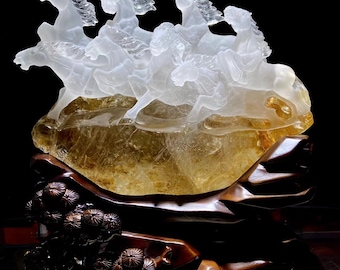 May include: A sculpture of five white horses carved from crystal, galloping across a golden brown mountain. The mountain is mounted on a dark brown wooden base with a carved floral design.