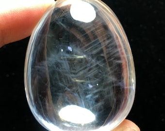 May include: A clear quartz crystal egg with white and gray inclusions. The egg is smooth and polished.