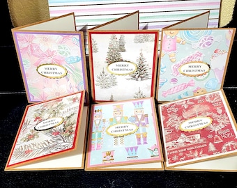 May include: A collection of six Christmas greeting cards with various festive designs. Each card features a decorative oval with the words "MERRY CHRISTMAS". The cards have different patterns, including floral, winter scenes, and nutcrackers.
