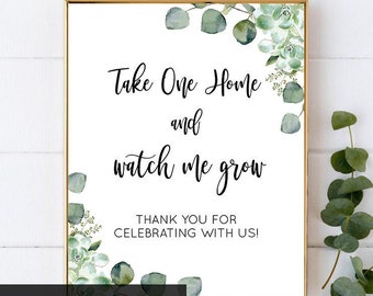 May include: A white sign with green foliage border, featuring the text "Take One Home and watch me grow". The sign also includes the text "Thank you for celebrating with us!" and the words "Matching Sign" at the bottom.